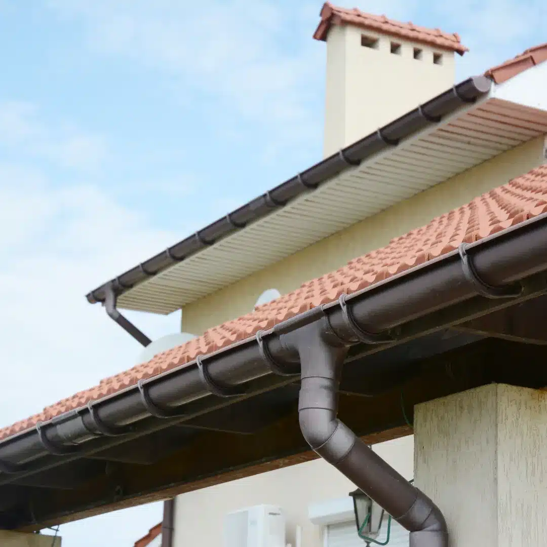 Dark brown half-round gutters and downspout system installed on a multi-level terracotta tile roof in Sydney.